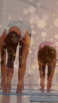 Vertical video: Coach leading fold while student mirroring on mats, bokeh aiding yoga stretch