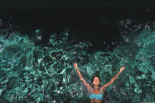 Woman with arms outstretched floating in villa pool, Uluwatu, Bali