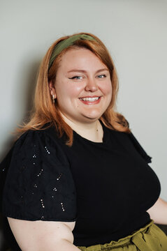 Young woman smiling at camera, black eyelet top, neutral background