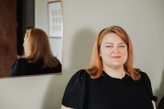 Woman smiling indoors with reflection in gold-framed mirror behind