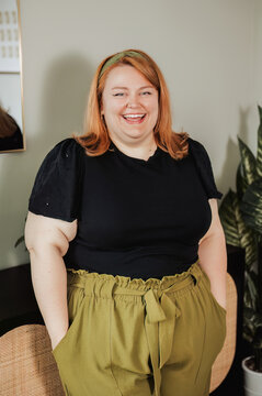 Plus size woman laughing, black top and olive pants