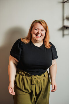Woman laughing in black top and olive pants near wall shelf