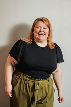 Plus size woman laughing, eyes closed, black top and olive pants