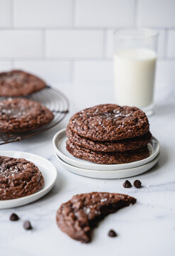 Plates of chocolate brownie cookies and milk on white background.