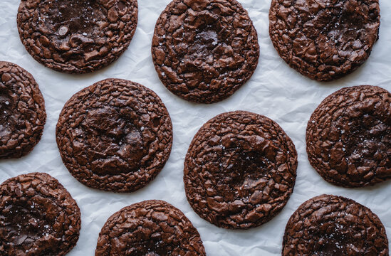 Top view of many chocolate brownie cookies on parchment paper.