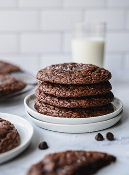 Plates of chocolate brownie cookies and milk on white background.