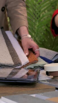 Materials coordinator arranging layout with wood tile and fabric samples on table, hands positioning laminate and marble pieces, experimenting with composition and contrast for client presentation
