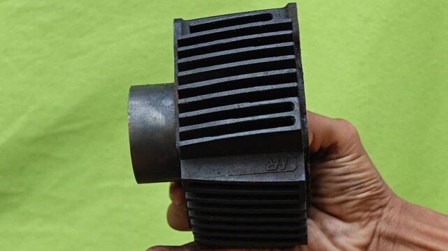 A man is holding Used black honda ex5 Motorcycle Engine Cylinder Block on green background. Mechanic and Spare Parts Concept.