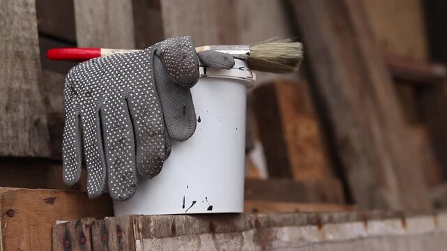 Painting set: brush, gloves and small white bucket with paint or varnish on wooden background. Workshop. Repair and construction concept. Painting tools on wooden background. Close-up of tools