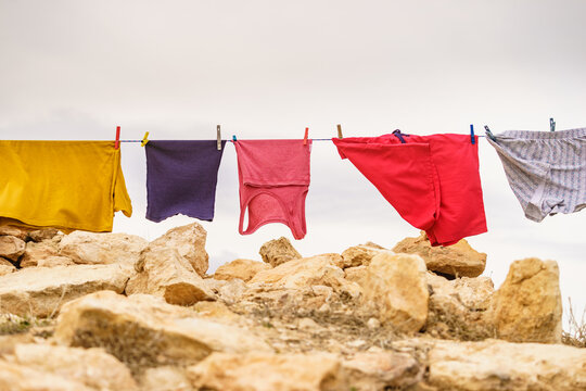 Clothes hang on a line over rocks in a dry area on a cloudy day while the wind moves them gently