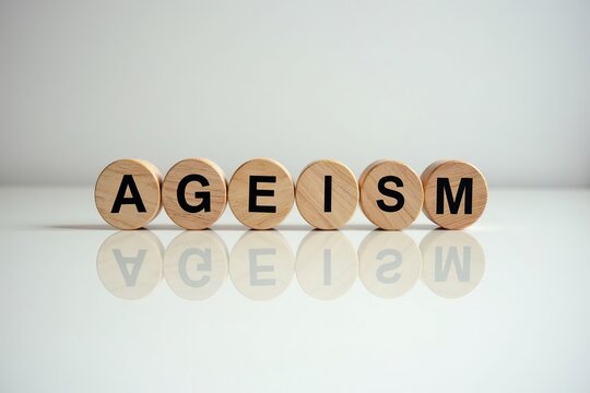 Symbolizing Ageism in the Workplace: Conceptual Image of Round Wooden Blocks with the Word Ageism on a Reflective White Desk