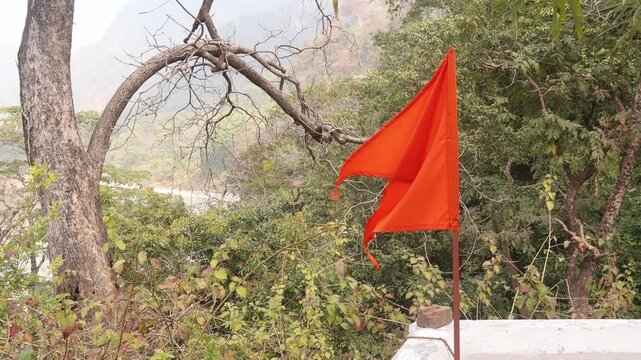 Raw 4K footage of a red religious flag at a temple in Uttarakhand, waving in forest surroundings, showing spiritual symbol and peaceful natural environment in India.