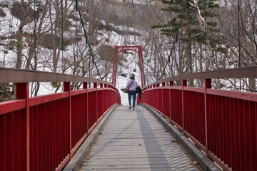 A woman walking across Futami Tsuribashi suspension bridge in Jozankei hot spring area, Sapporo, Japan during early spring season © AllanJoseph