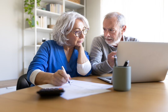 Senior couple doing home finances using laptop and calculator