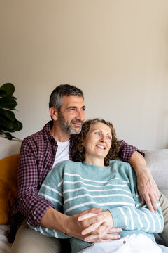 Cheerful middle-aged couple relaxing on sofa embracing at home