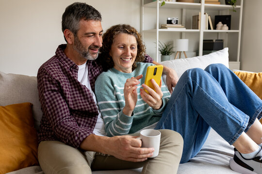 Mature couple relaxing on sofa using mobile phone