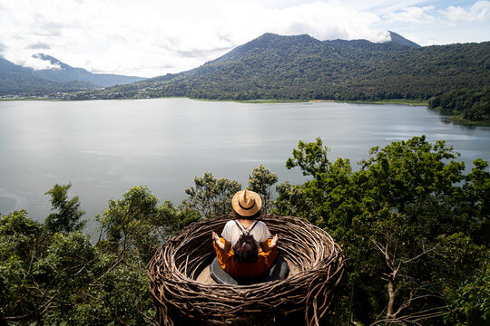 Woman meditating in bird's nest overlooking bali lake