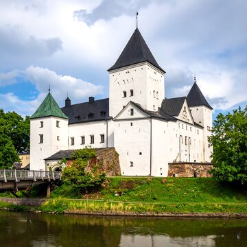 Historic white castle with green and black turrets, bridge over water