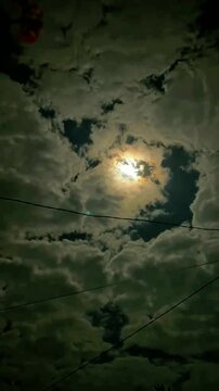 A luminous glow pierces through a dense layer of clouds, casting an ethereal light across the sky, with power lines subtly crossing the foreground.