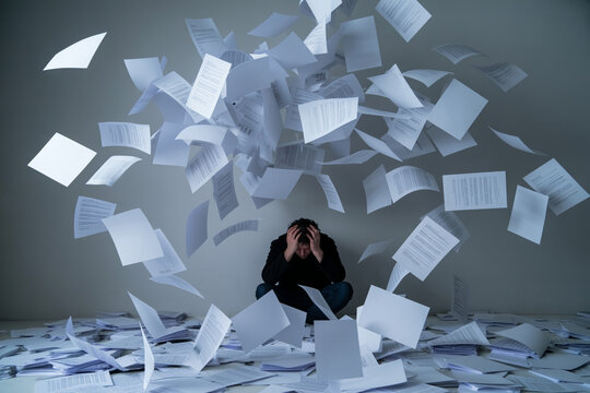 Stressed man sitting on the floor surrounded by a whirlwind of flying documents