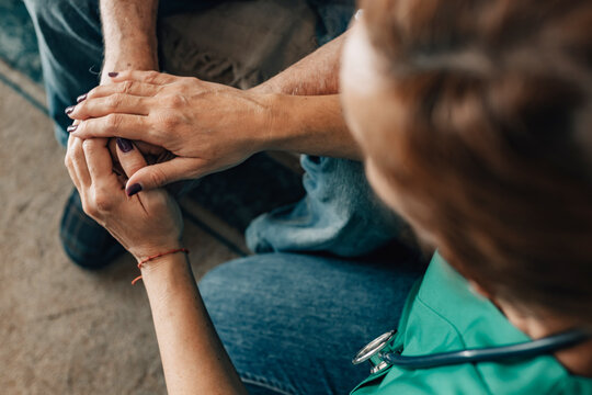 nurse in green scrubs gently holding elderly patient hands, showing empathy, care and emotional support during medical consultation