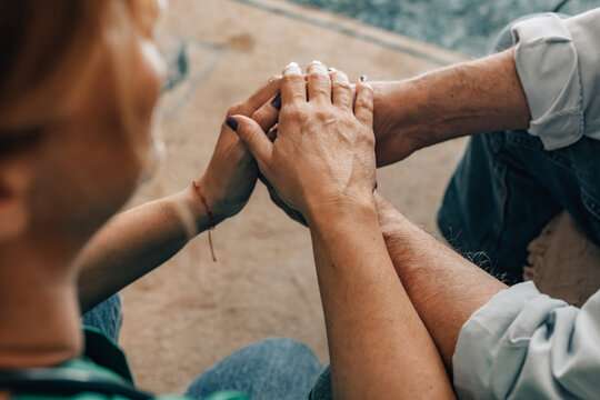 Close-up of two people holding hands outdoors, conveying empathy, support, and human connection. Red bracelet detail adds intimacy to this emotional moment
