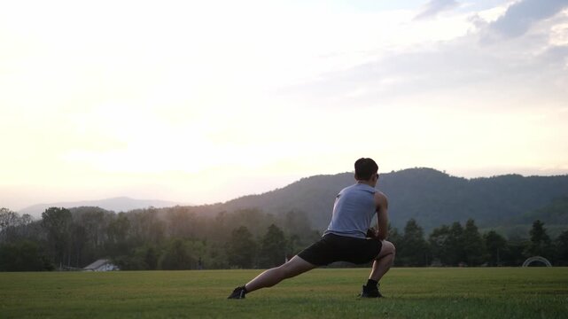 Cinematic back view of a male athlete performing a standing full body stretch in a park, scenic mountain landscape at sunset background, wellness and healthy lifestyle concept