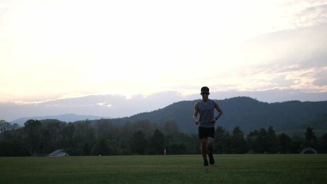 Cinematic shot of a male athlete running towards the camera in an outdoor setting, beautiful mountain landscape background during blue hour, fitness and perseverance concept