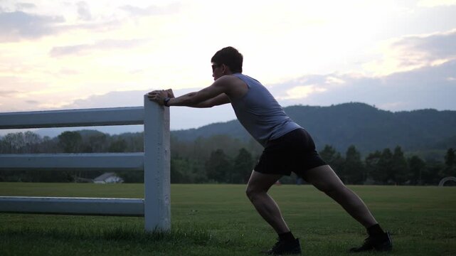 Cinematic back view of a male athlete performing a standing full body stretch in a park, scenic mountain landscape at sunset background, wellness and healthy lifestyle concept