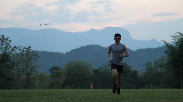 Cinematic shot of a male athlete running towards the camera in an outdoor setting, beautiful mountain landscape background during blue hour, fitness and perseverance concept