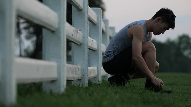 Cinematic shot of a male athlete tying his shoelaces before a workout in a park, preparing for a run during sunset, fitness and healthy lifestyle concept
