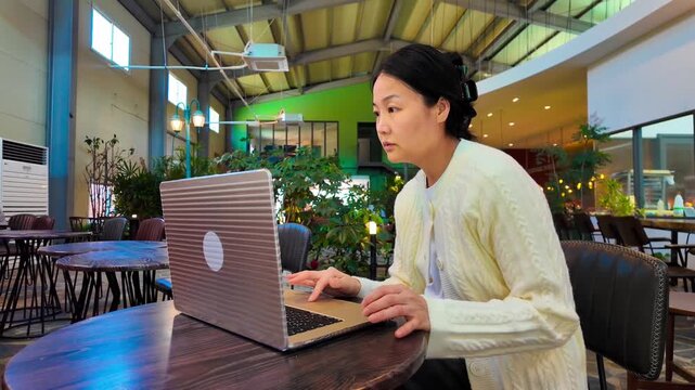 A stressed woman in a caffe is focused on her laptop