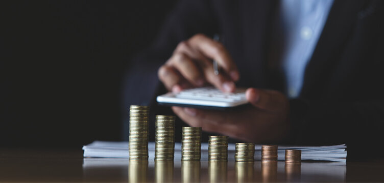 Businessman calculating finances with stacked coins and calculator, representing budgeting, financial analysis, and business accounting