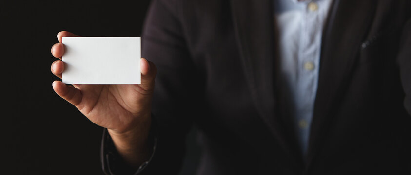 Businessman holding blank white business card with copy space on dark background, ideal for branding, corporate identity, marketing, and presentation design