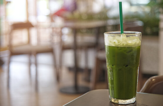 Iced matcha green tea latte in a glass with straw on table in cafe, soft light and blurred background with copy space