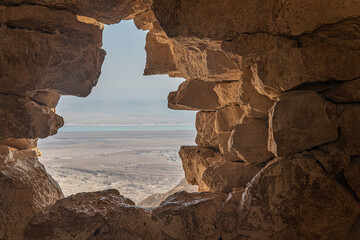 View from ancient stone wall of Masada fortress overlooking the Dead Sea and Judean Desert, Israel. Historic ruins framing desert landscape with natural light. © Mariia