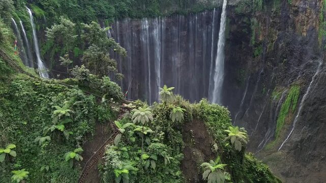 Beautiful cinematic footage of Coban Sewu or Tumpak Sewu Waterfall, a famous landmark in Lumajang, Indonesia. Wide shot of thousand waterfalls surrounded by dense green forest and tropical plants.