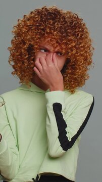 Exhausted tired teenager school girl with curly frizzy hairstyle takes off glasses, feels eyes pain, being overwork burnout from long hours studying or working. Child kid isolated on gray background.