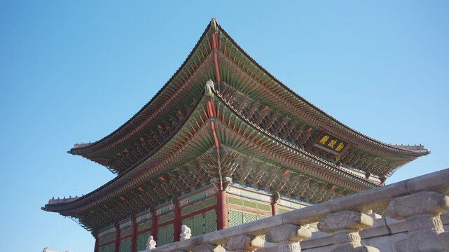 Gyeongbokgung Palace throne hall rises majestically against a clear blue sky in Seoul, South Korea, featuring ornate double-tiered roofing with intricate wooden brackets and stone balustrades.