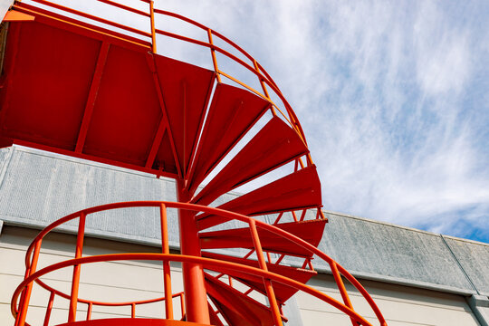 An industrial setting features a vibrant orange metal spiral staircase leading up to an elevated factory platform.