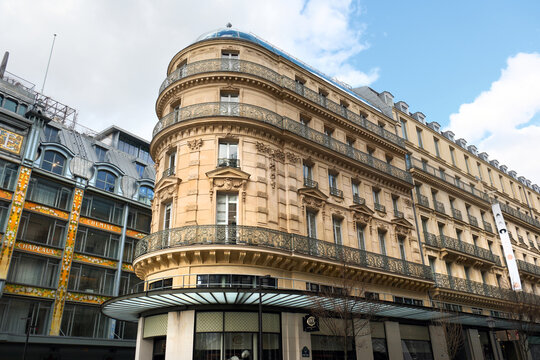 Paris, France - March 9, 2026. The ornate Haussmann-style architecture of historic apartment buildings stands on a street corner in Paris, featuring wrought-iron balconies and a cloudy sky.