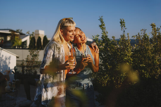 Happy young women embracing enjoying cocktails on rooftop