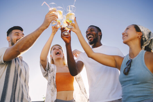 Diverse friends cheering with cocktails having fun outdoors