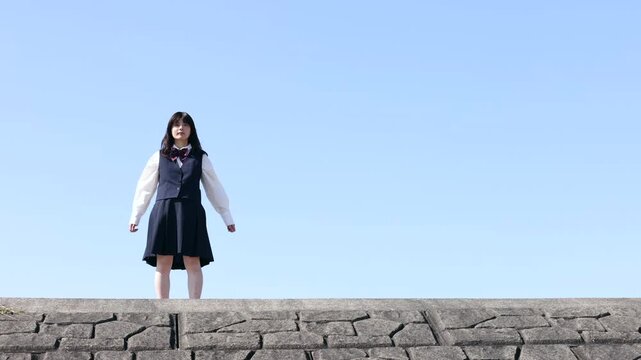 青空に向かってジャンプする笑顔の女子高校生