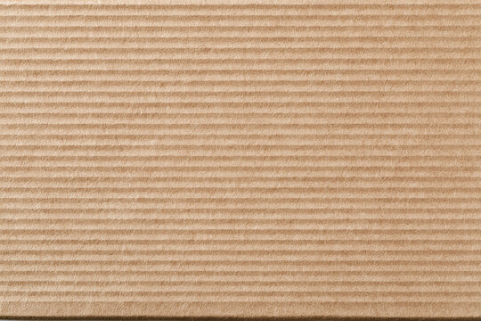 Detailed close-up texture of recycled brown corrugated cardboard packaging material featuring horizontal ridges and a natural organic fibrous surface for background and design.