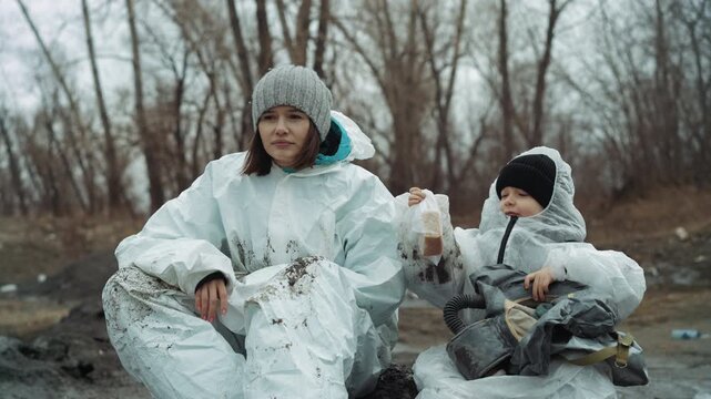 White woman and child sharing food, volunteer passing wrapped sandwich, child accepting with cautious smile, both in white protective suits and knitted hats, muddy roadside camp, leafless trees, quiet