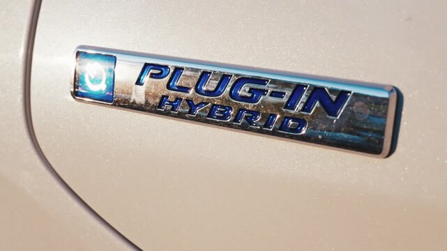 Plug in hybrid badge on car side close up shot showing silver metallic emblem for eco friendly auto.