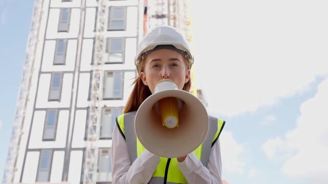 Young woman directs workers on a construction site with a megaphone on a sunny day in the city