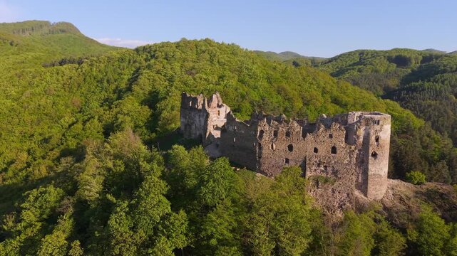 Stunning aerial view orbiting the medieval Sasovsky Castle ruins. The historic fortress stands majestically on a hilltop surrounded by a lush forest
