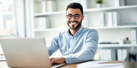 Obraz premium Young handsome Middle Eastern man working on a laptop in a bright office setting